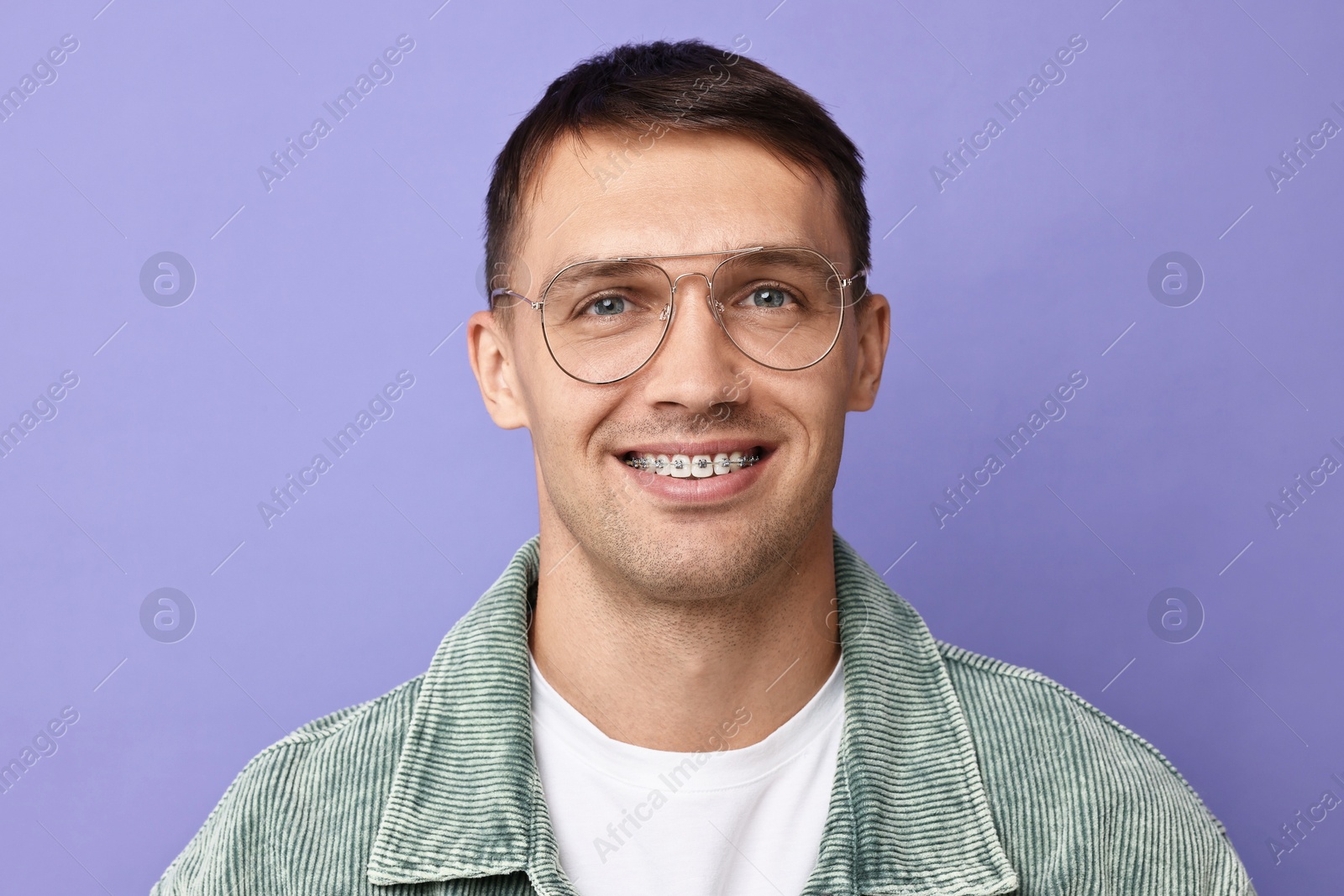 Photo of Smiling man with dental braces on violet background