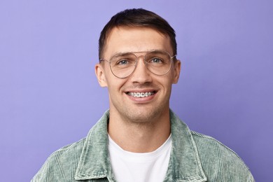 Smiling man with dental braces on violet background