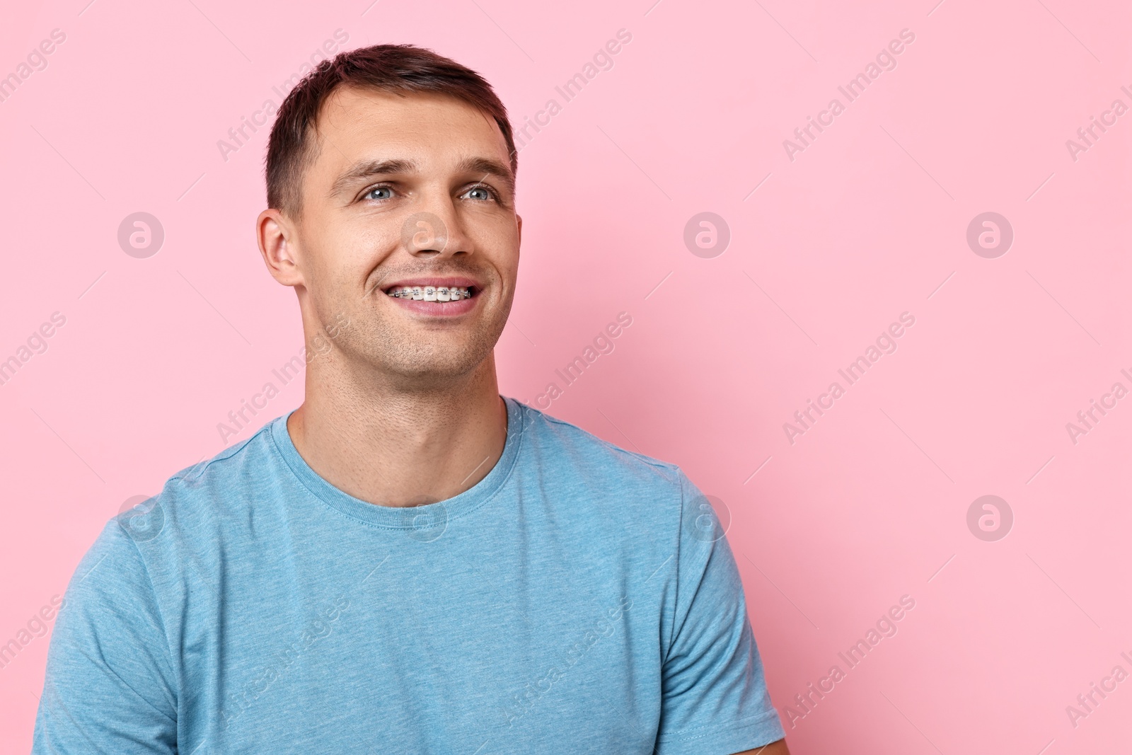 Photo of Smiling man with dental braces on pink background. Space for text