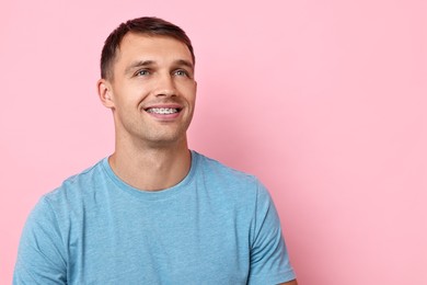 Photo of Smiling man with dental braces on pink background. Space for text