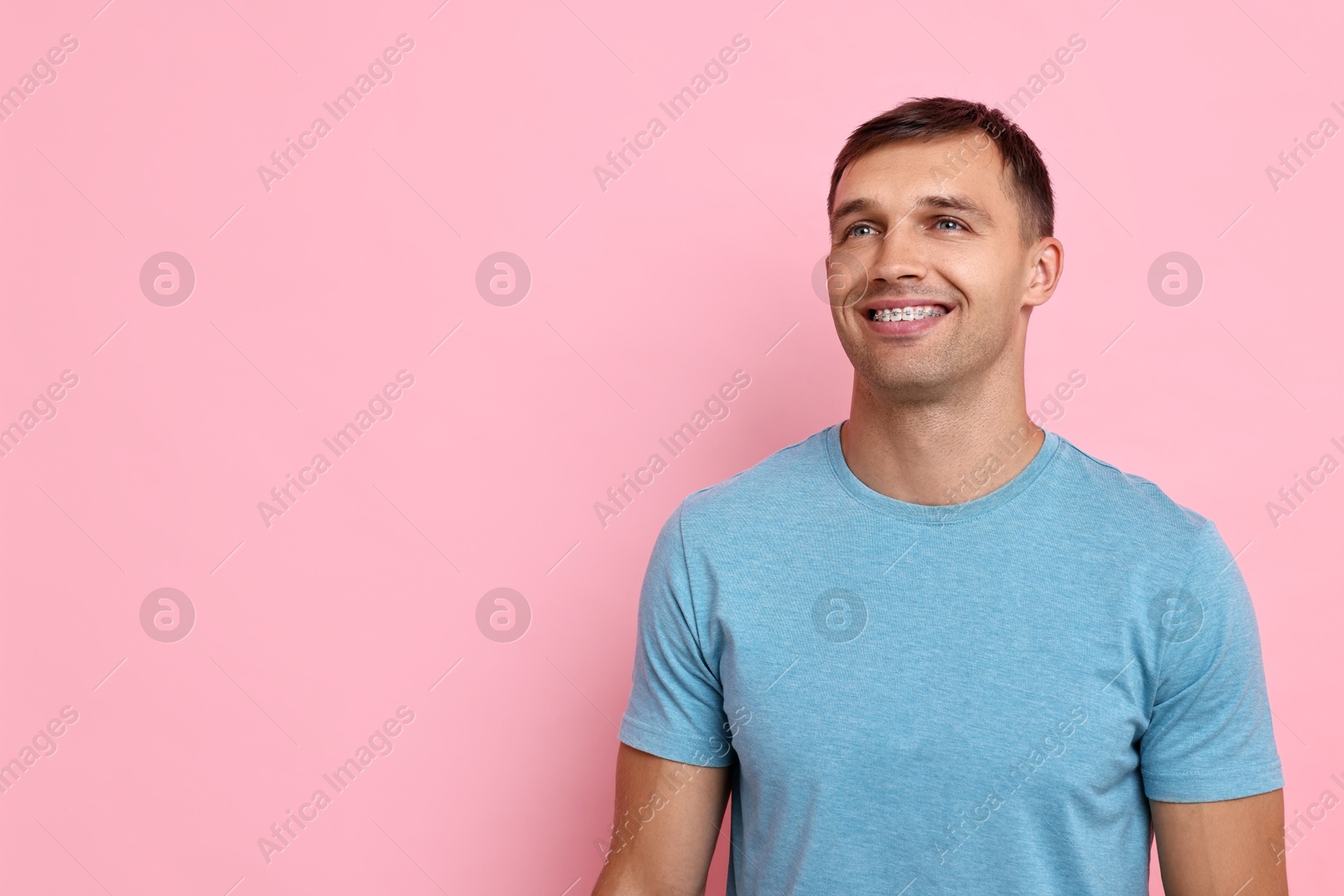 Photo of Smiling man with dental braces on pink background. Space for text