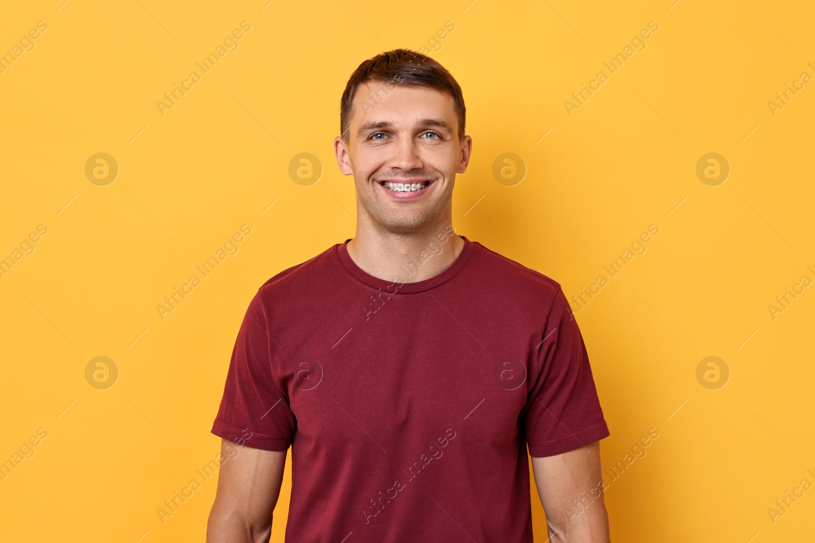 Photo of Smiling man with dental braces on yellow background