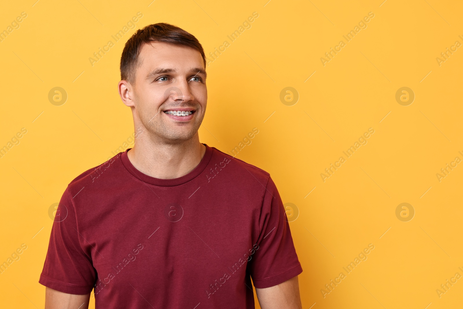 Photo of Smiling man with dental braces on yellow background. Space for text