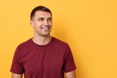 Smiling man with dental braces on yellow background. Space for text