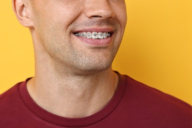 Smiling man with dental braces on yellow background, closeup