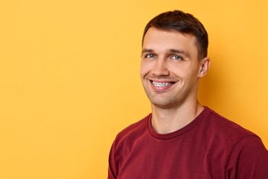 Smiling man with dental braces on yellow background. Space for text