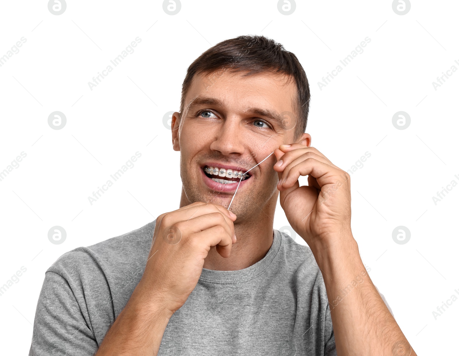 Photo of Man with braces cleaning teeth using dental floss on white background