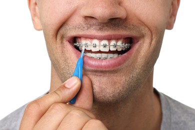 Man with dental braces cleaning teeth using interdental brush on white background, closeup