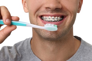 Man with dental braces cleaning teeth on white background, closeup