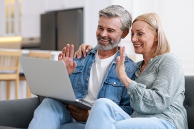 Happy middle aged couple having video chat via laptop on sofa indoors