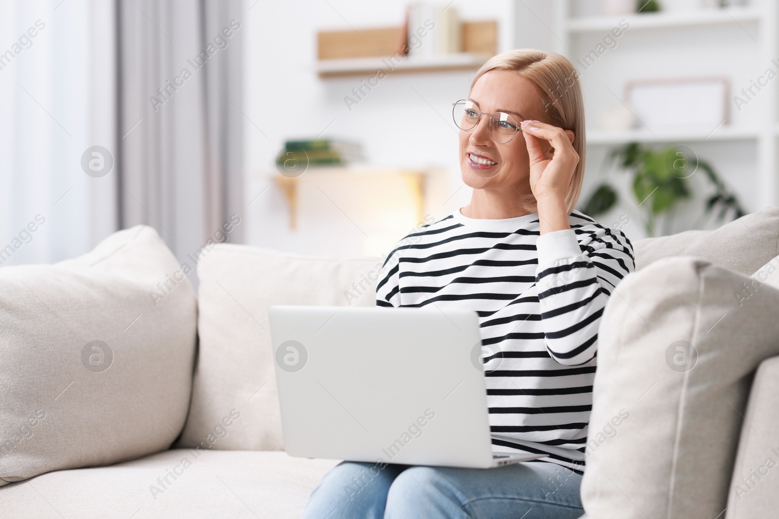 Photo of Happy middle aged woman using laptop on sofa at home