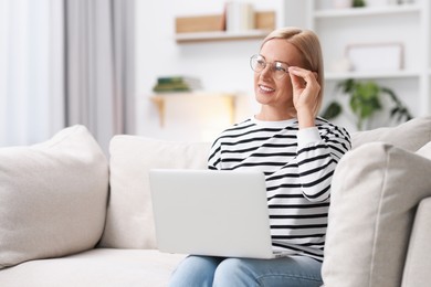 Happy middle aged woman using laptop on sofa at home