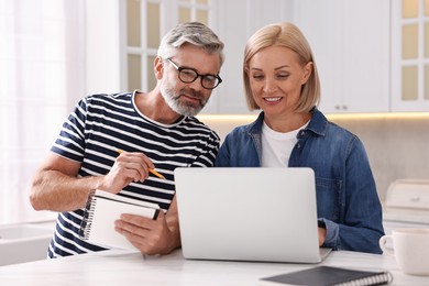 Middle aged couple working at white marble table in kitchen