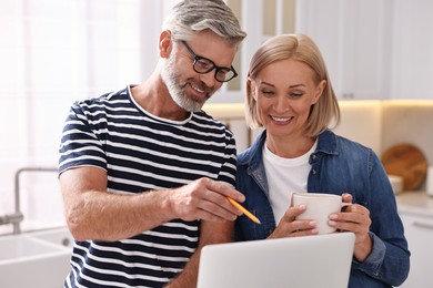 Happy middle aged couple using laptop in kitchen