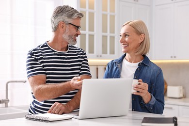 Photo of Happy middle aged couple working at white marble table in kitchen