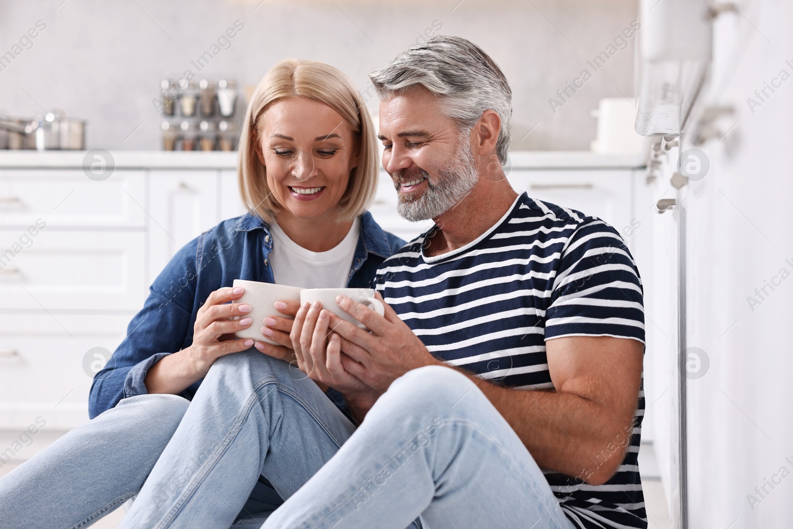 Photo of Happy middle aged couple with cups of drink in kitchen