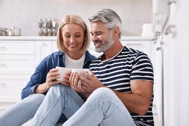 Happy middle aged couple with cups of drink in kitchen