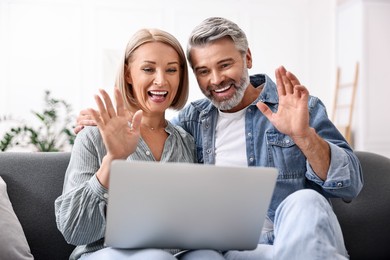 Happy middle aged couple having video chat via laptop on sofa indoors