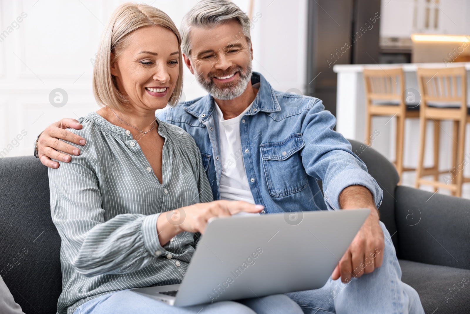 Photo of Happy middle aged couple using laptop on sofa in kitchen