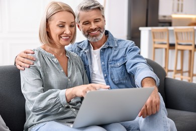 Happy middle aged couple using laptop on sofa in kitchen