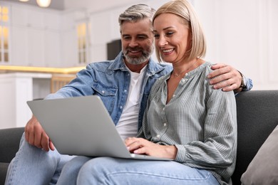 Happy middle aged couple using laptop on sofa in kitchen