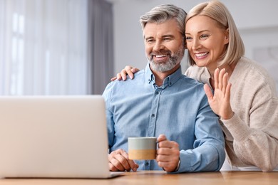 Photo of Happy middle aged couple having video chat via laptop at table indoors