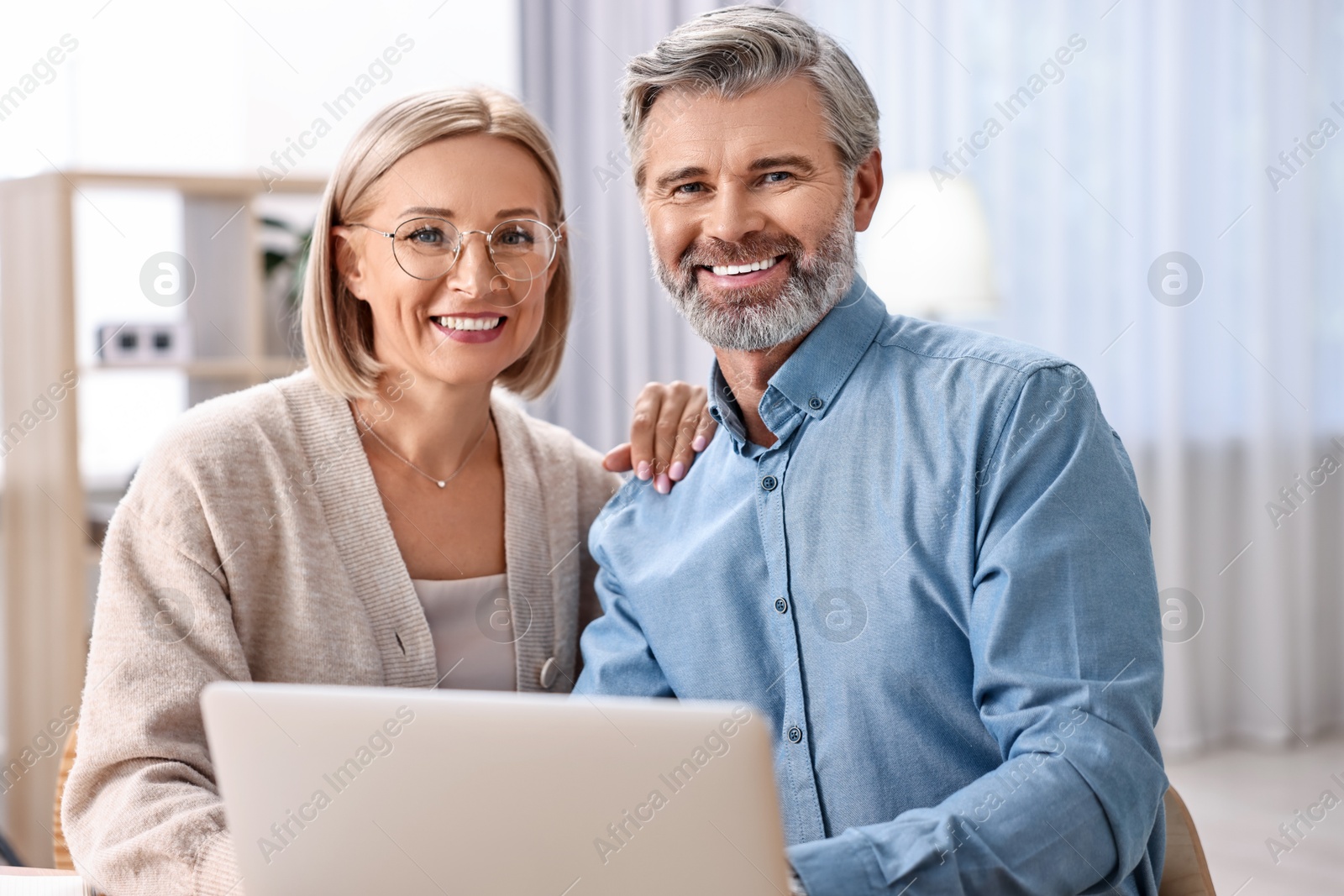 Photo of Happy middle aged couple using laptop at home