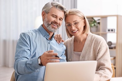 Photo of Happy middle aged couple using laptop at home