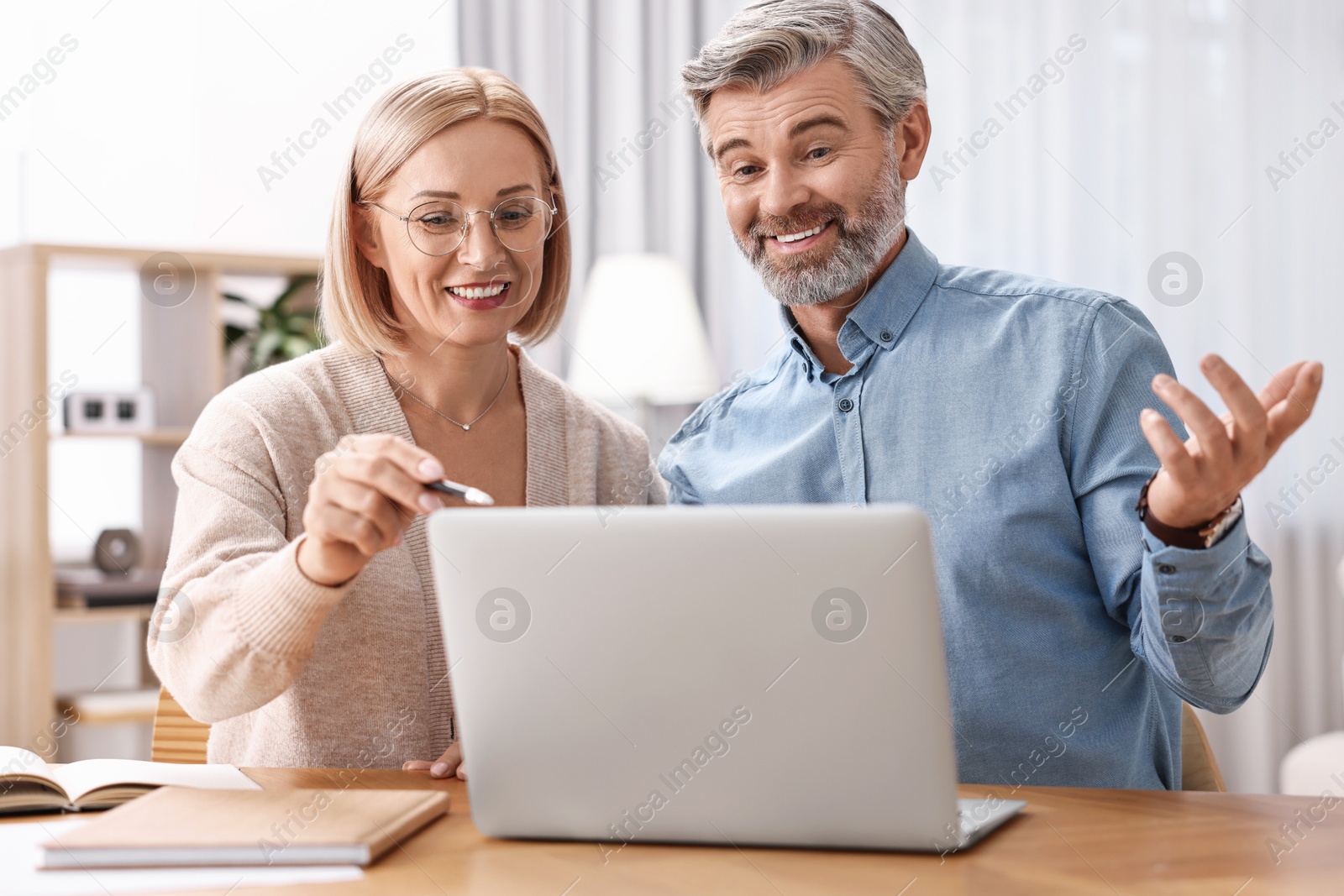 Photo of Happy middle aged couple working with laptop at wooden table indoors