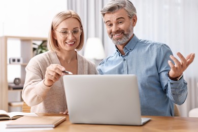 Happy middle aged couple working with laptop at wooden table indoors