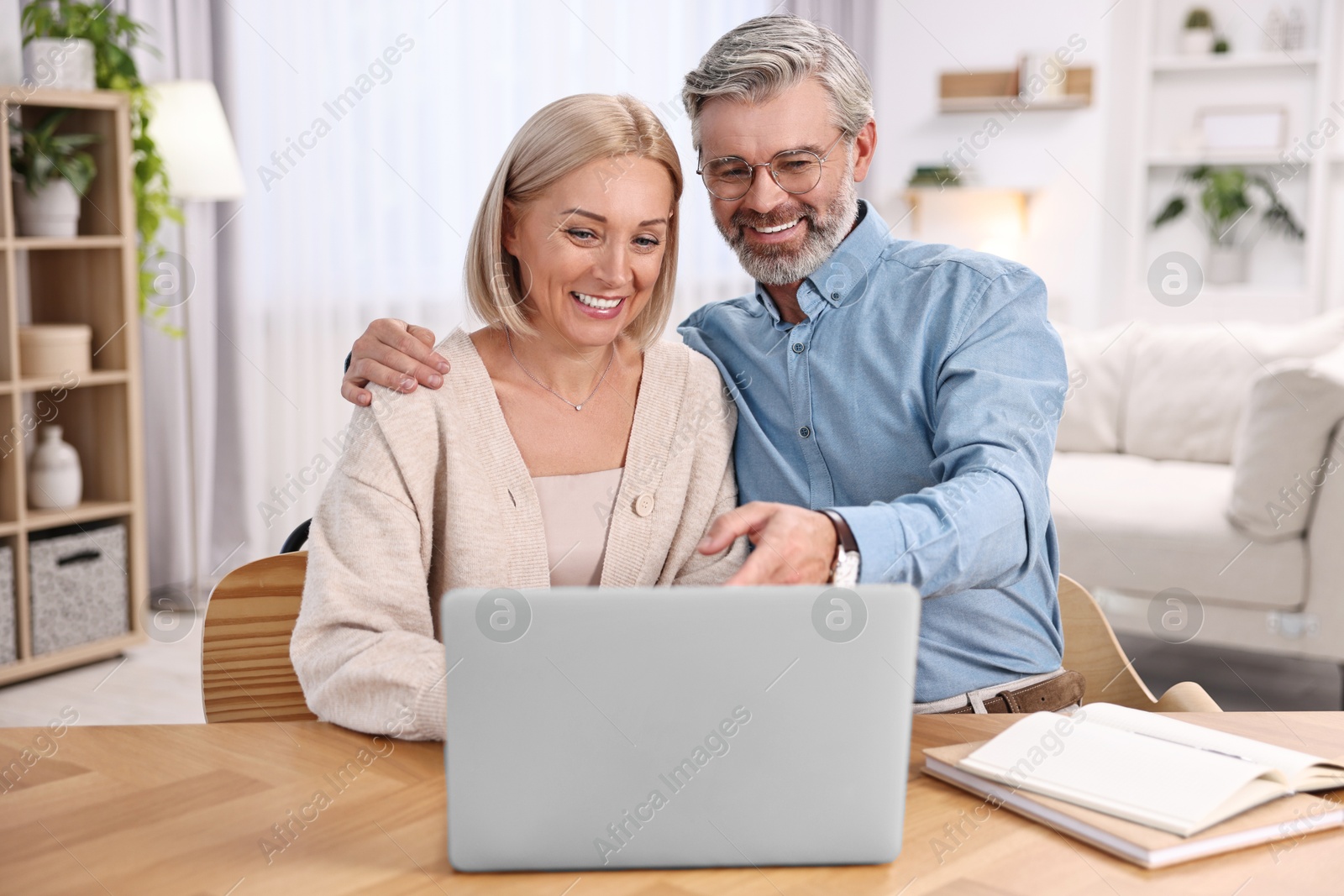 Photo of Happy middle aged couple using laptop at wooden table indoors