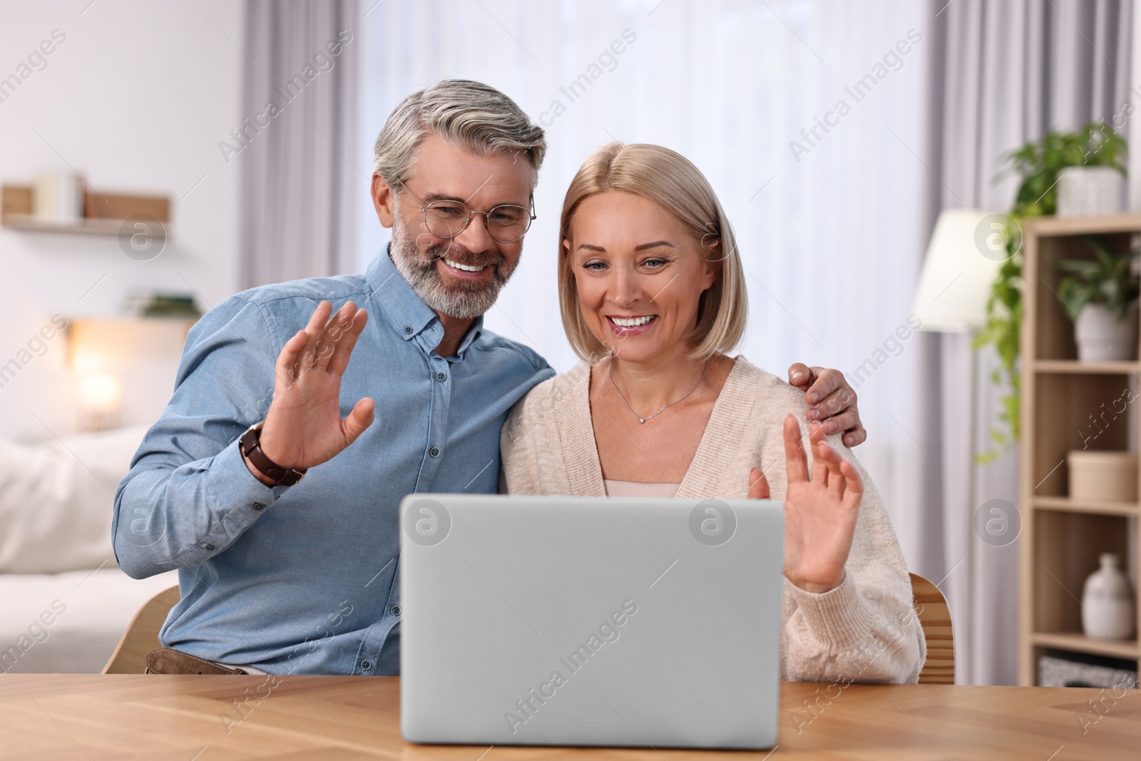 Photo of Happy middle aged couple having video chat via laptop at wooden table indoors