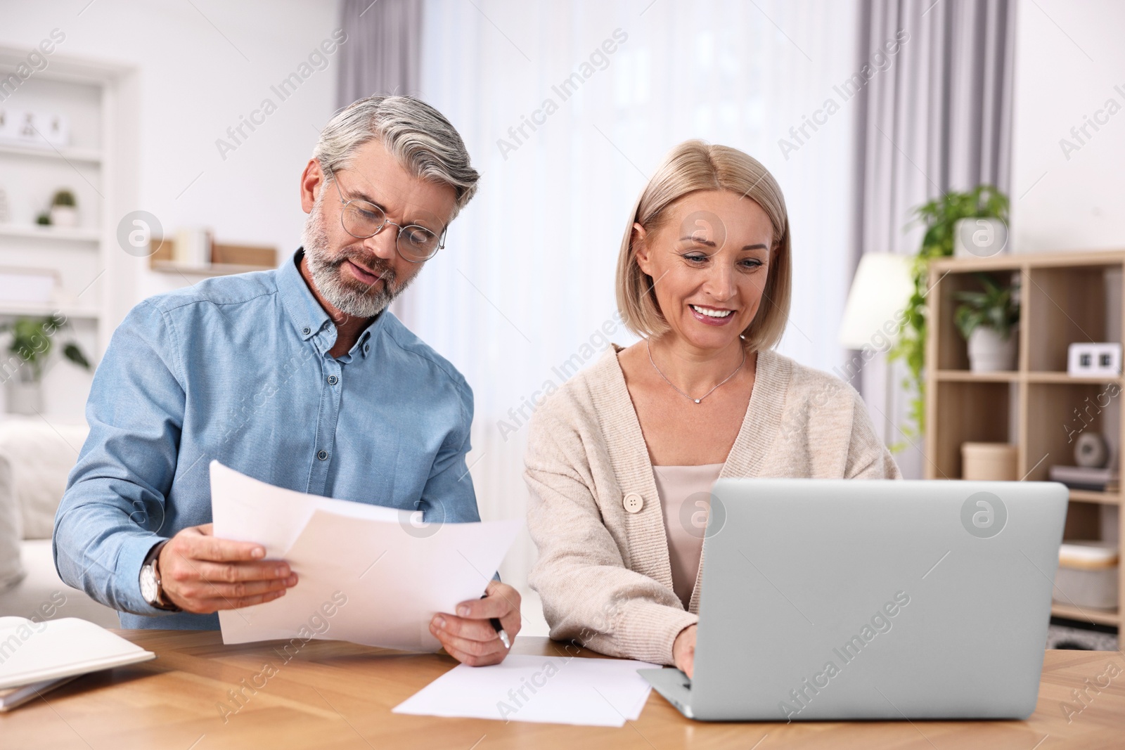 Photo of Happy middle aged couple working at wooden table indoors