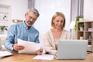 Happy middle aged couple working at wooden table indoors