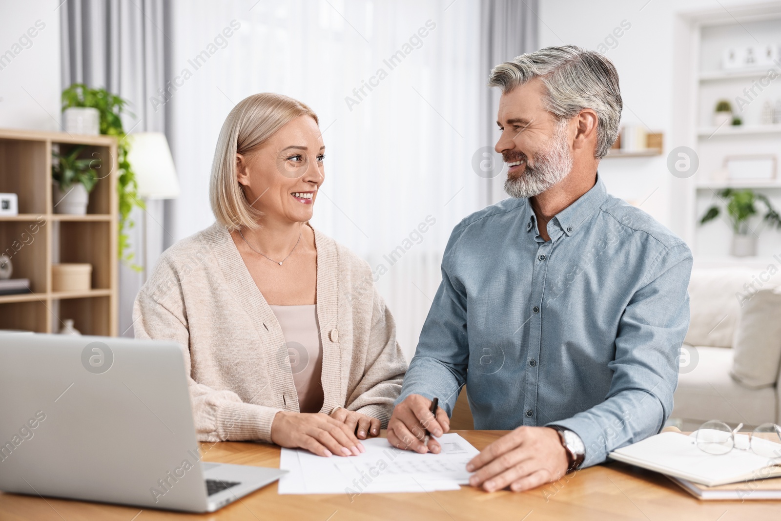 Photo of Happy middle aged couple working at wooden table indoors