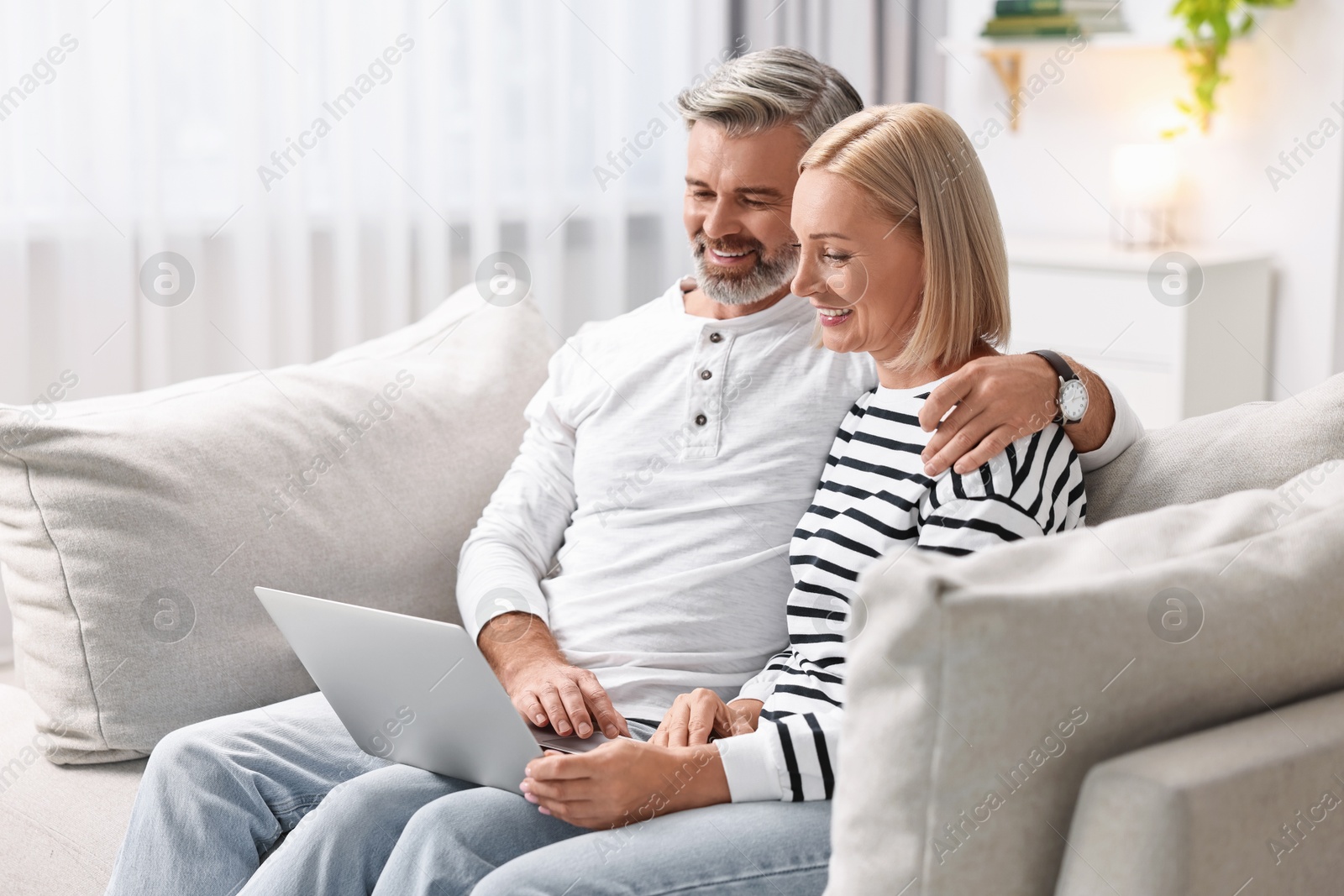 Photo of Happy middle aged couple using laptop on sofa at home