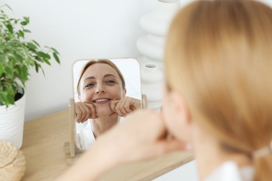 Smiling woman doing facial self massage near mirror at home