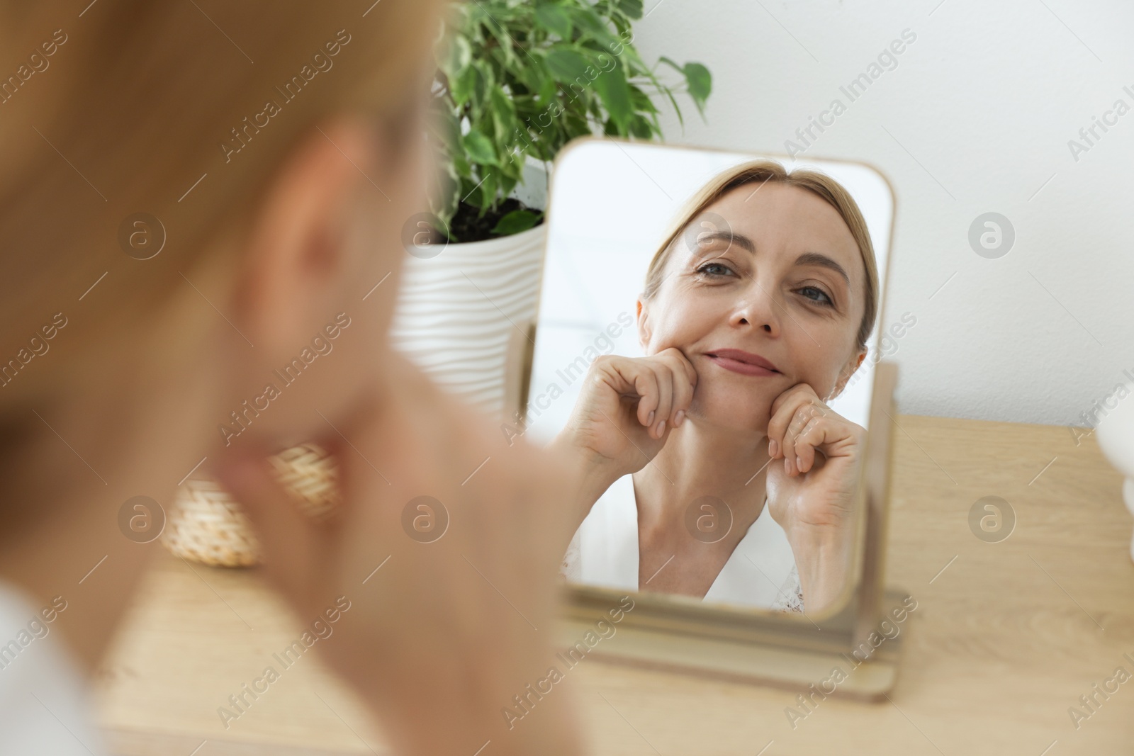 Photo of Beautiful woman doing facial self massage near mirror at home