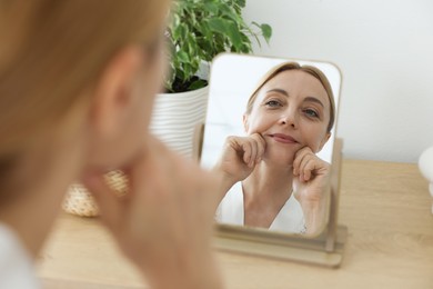 Beautiful woman doing facial self massage near mirror at home