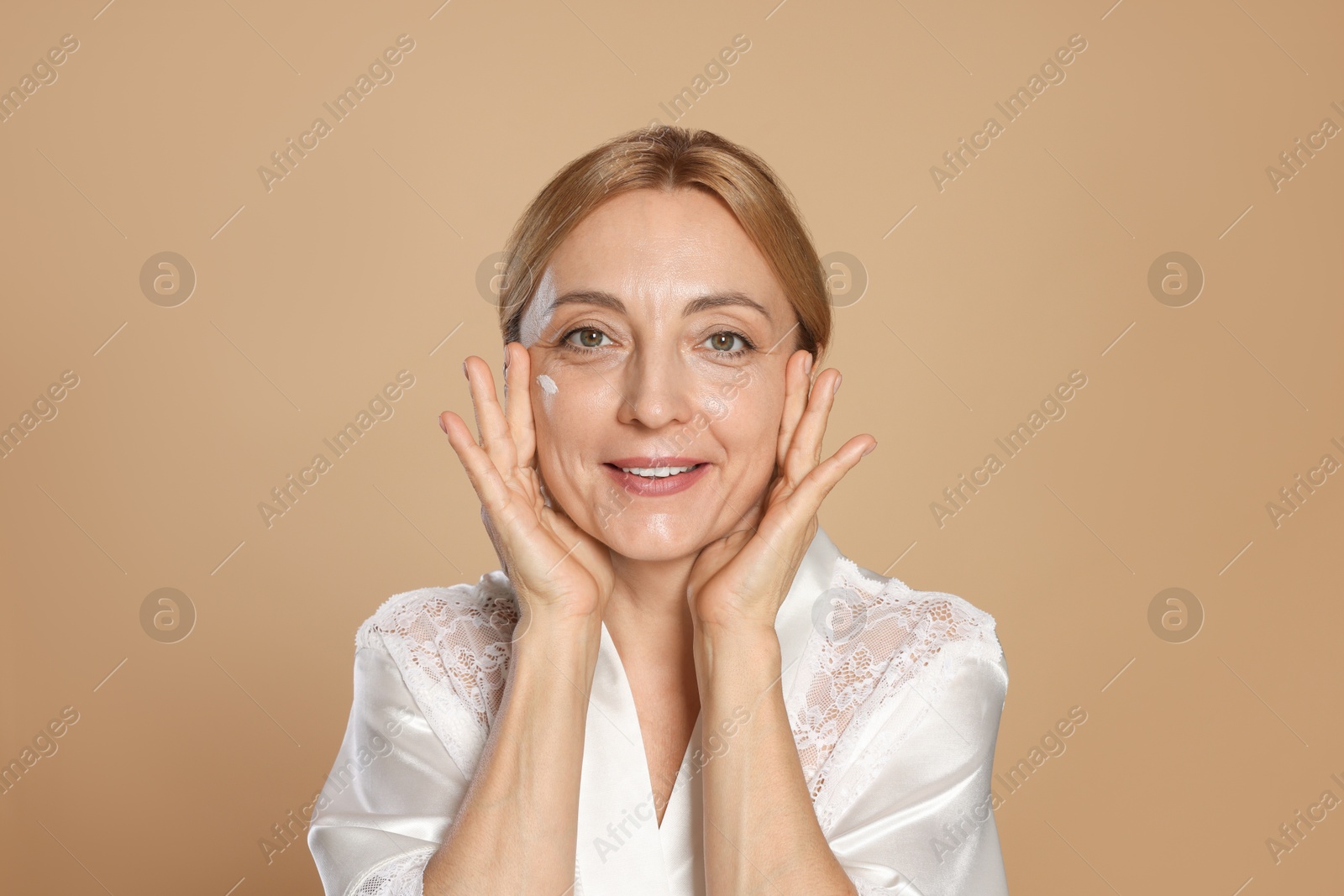 Photo of Smiling woman with cream on face against beige background