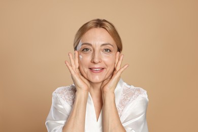 Smiling woman with cream on face against beige background