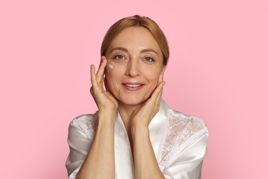 Photo of Smiling woman with cream on face against pink background