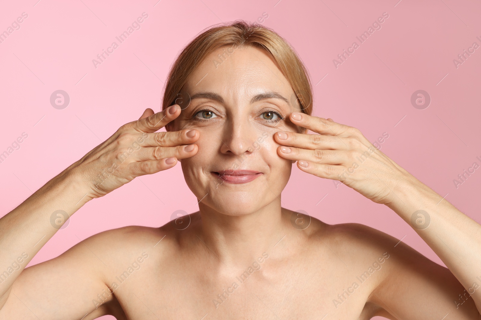 Photo of Beautiful woman doing facial self massage on pink background