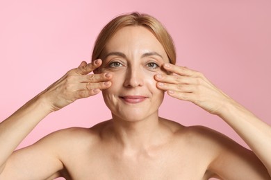 Beautiful woman doing facial self massage on pink background