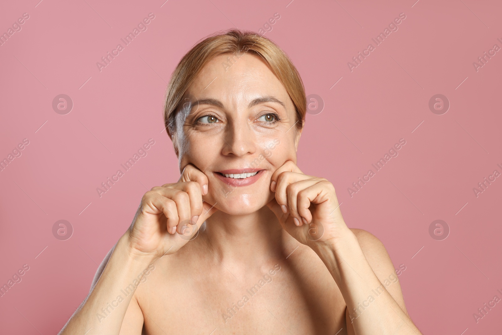 Photo of Smiling woman doing facial self massage on pink background