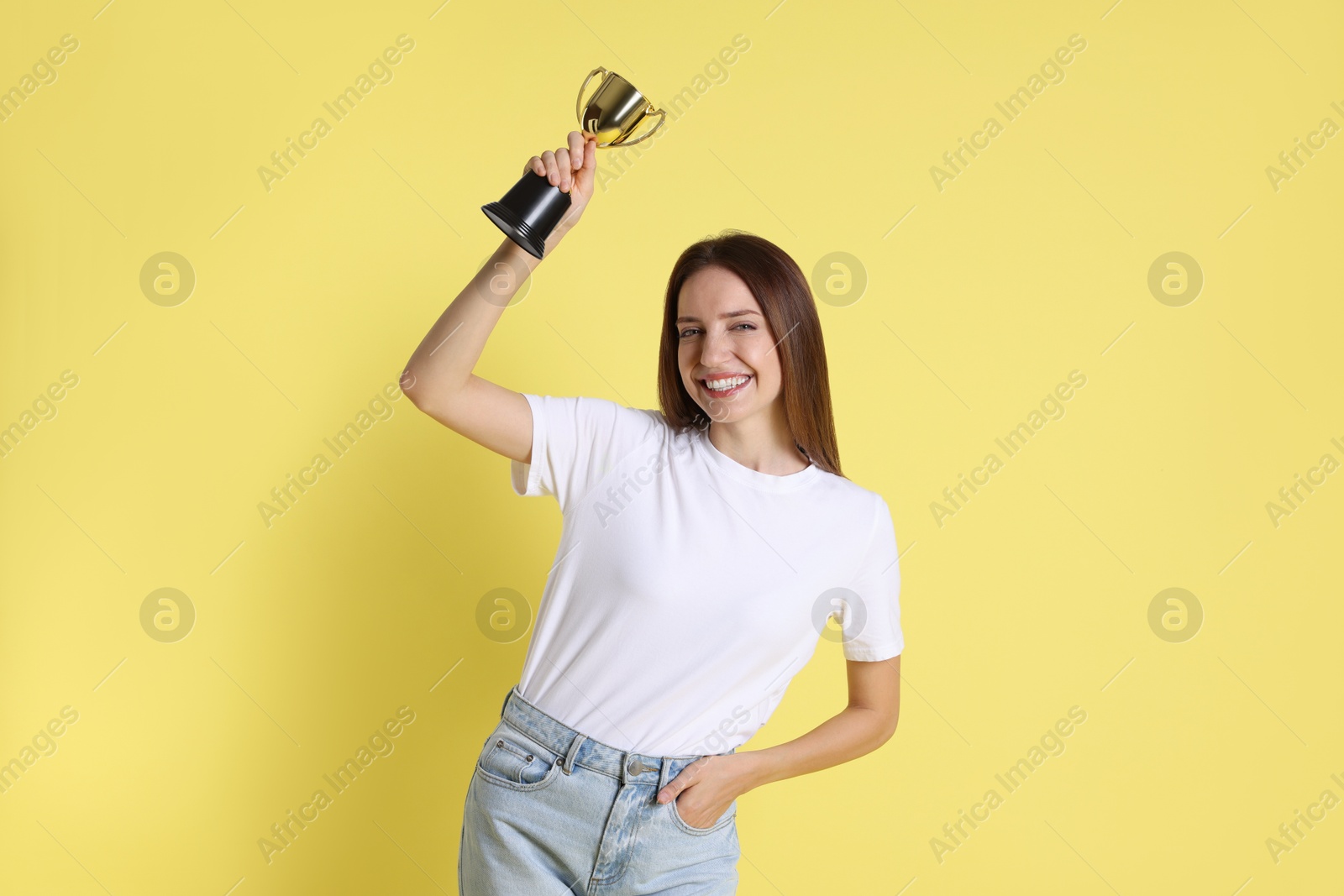 Photo of Happy winner with gold trophy cup on yellow background