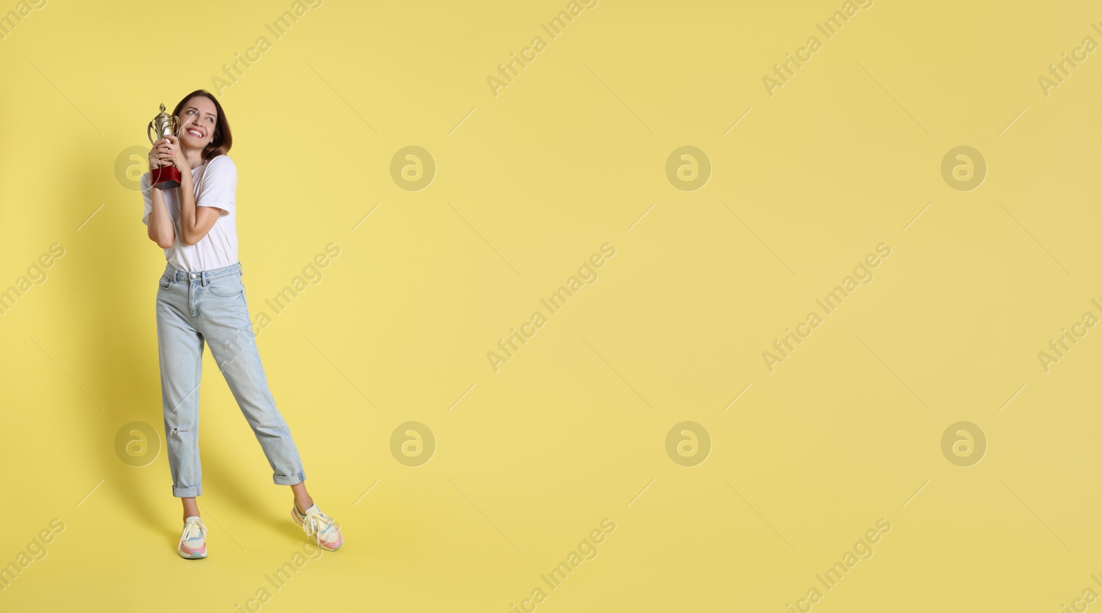 Photo of Happy winner with gold trophy cup on yellow background