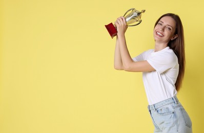 Photo of Happy winner with gold trophy cup on yellow background, space for text