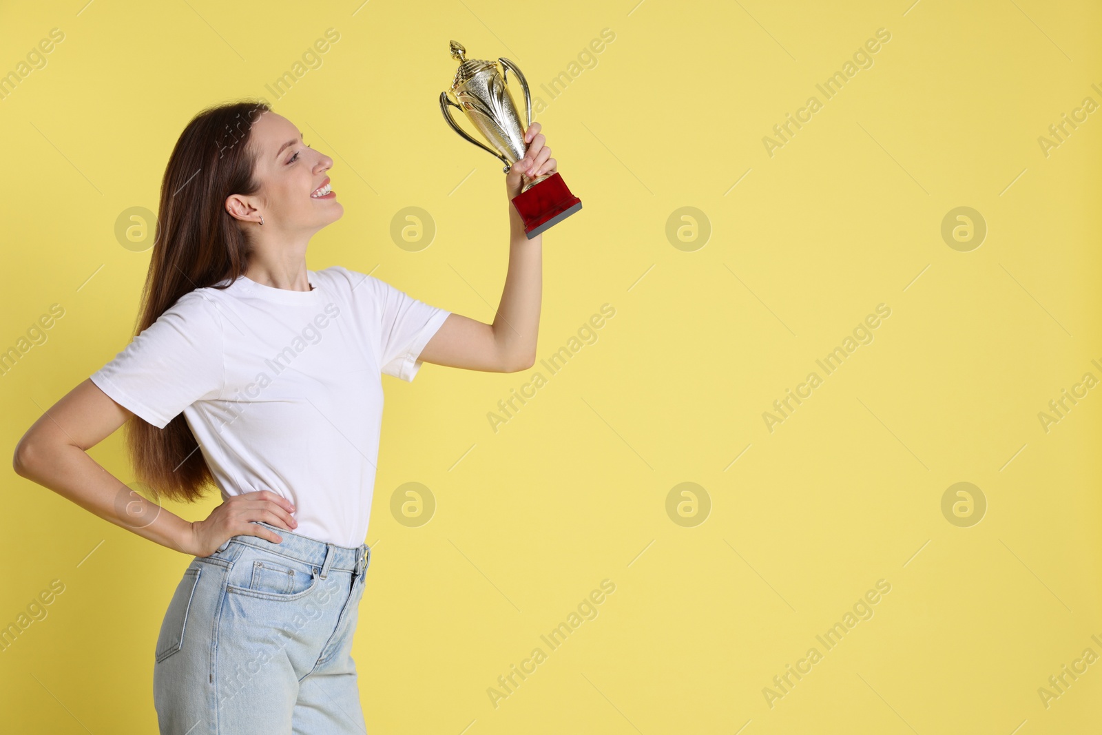 Photo of Happy winner with gold trophy cup on yellow background, space for text