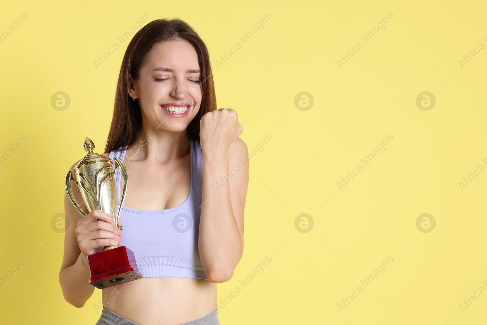 Photo of Happy winner with gold trophy cup on yellow background, space for text